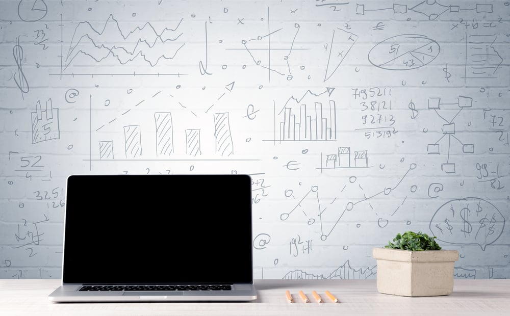 A professional laptop with blank screen sitting on a white office desk in front of wall full of pie charts, calculations and graphs concept