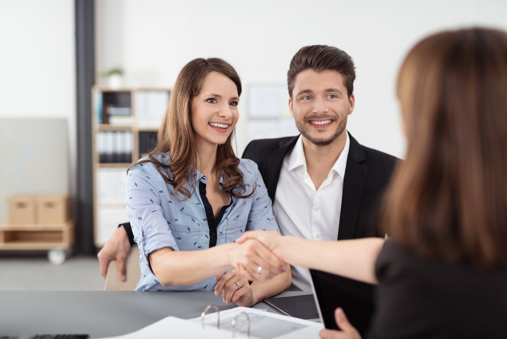 Happy Young Professional Couple Shaking Hands with a Real Estate Agent After Some Business Discussions Inside the Office.-1