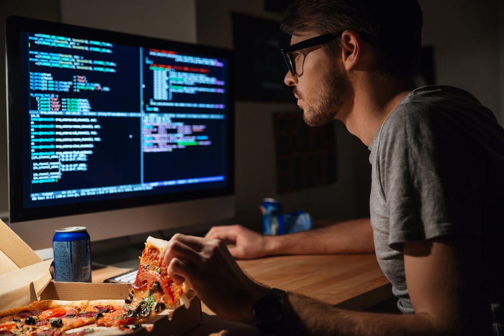 Profile of concentrated young software developer eating pizza and coding at home-1