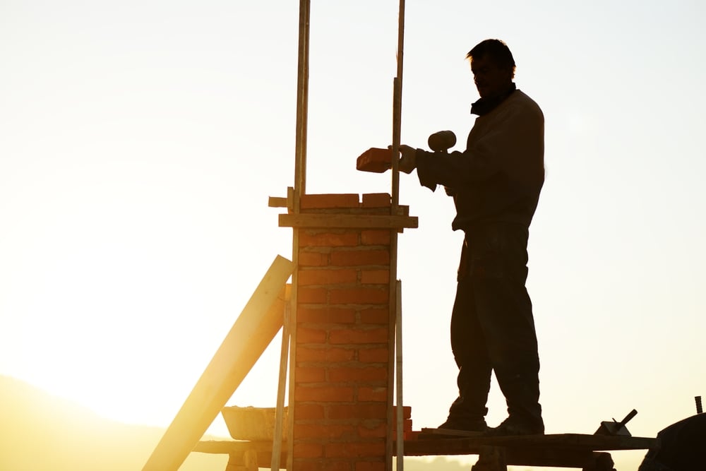 Silhouette of worker building a chimney on new house