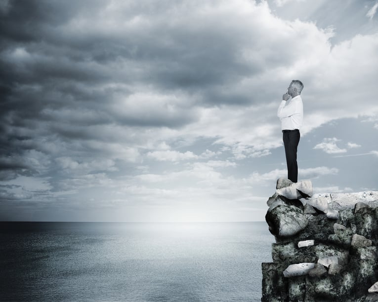 Thoughtful businessman standing at the edge of a cliff with the sea on the background