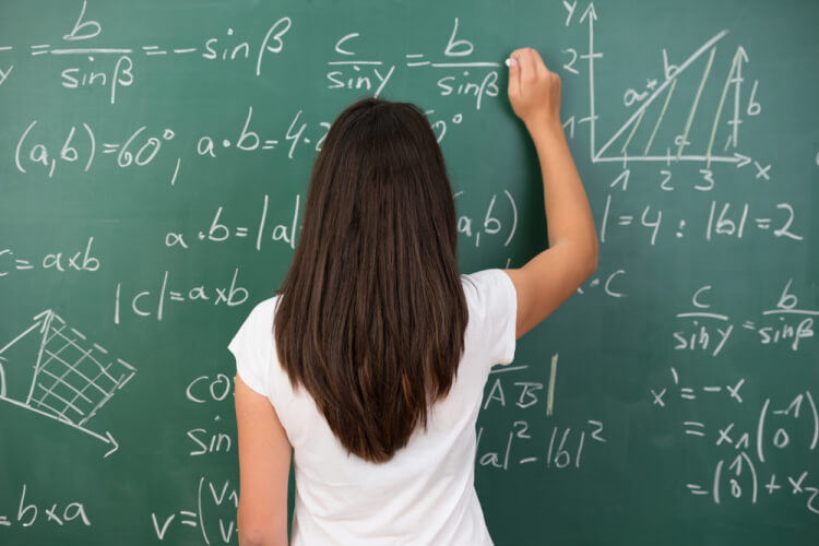 Clever young woman solving a mathematical problem standing with her back to the camera writing on a college blackboard